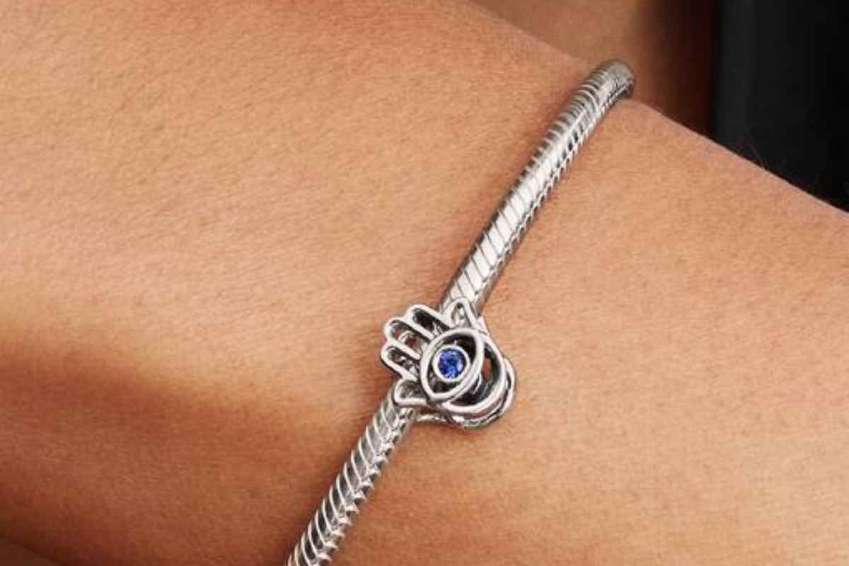 mano con pietra blu sopra, charm su bracciale legato ad un polso