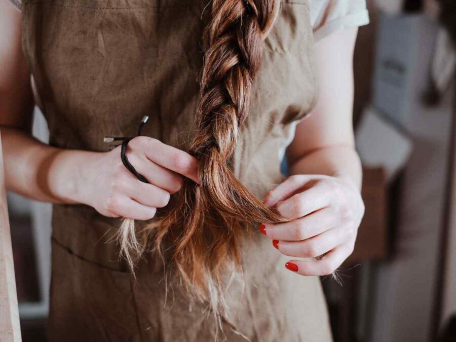 ragazza intreccia capelli con elastico in mano